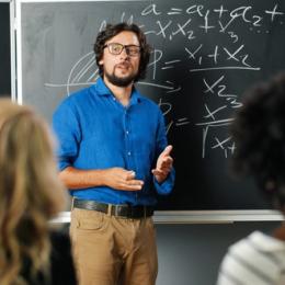 Nauczyciel stojący pod tablicą, uczący matematyki.